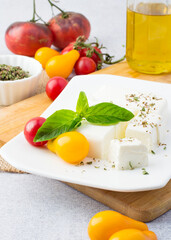 Feta on a plate with basil, yellow and red tomatoes on the kitchen table. Cooking.