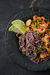 Close-up view of a plate with spicy black rice noodles, shrimps and mushrooms