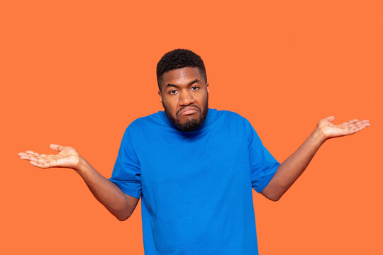 Man Wearing Blue Shirt Shrugging Shoulders Against Vibrant Orange Background Displaying Confusion or Indecision During Late Afternoon