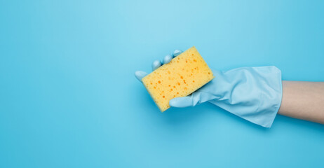 Womans hand in rubber glove holds yellow dishwashing sponge. House cleaning. Copy space
