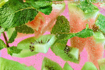 Fresh watermelon and tropical kiwi with green mint leaves, immersed in sparkling bubbles....