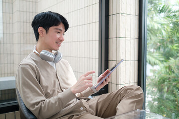 Young man is seated comfortably in a modern café, engrossed in using a tablet.