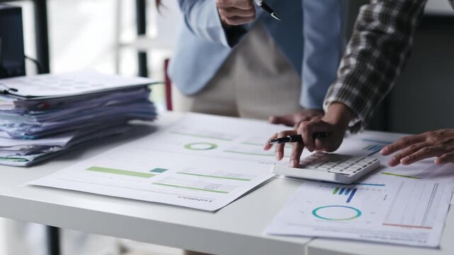 Business colleagues analyzing financial data, discussing charts and graphs, using a calculator, and collaborating on reports in a modern office setting