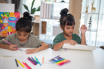 Two young girls are sitting at a table with pencils and coloring books