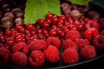 Tasty fresh ripe raspberry, red currant, gooseberry. Nutrients, Healthy berry texture on dark background. Red summer berries on black plate, high quality photo