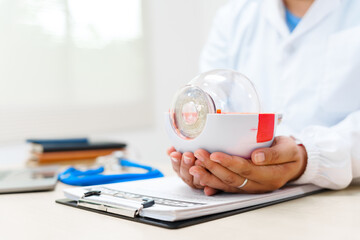 An eye doctor examines an anatomical model of the eye at the clinic, focusing on lens structure,...