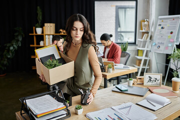Woman in stylish attire pack up belongings amid an office layoff, colleagues on backdrop.