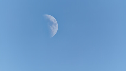 Portrait of the moon at midday in a cloud-free but hazy summer sky.