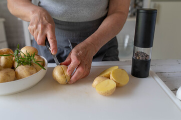 Woman cutting raw and fresh potatoes in halves on a cutting board in the kitchen