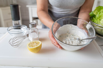 Woman preparing a healthy homemade salad dressing for green lettuce in the kitchen