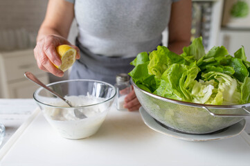 Woman preparing a healthy homemade salad dressing for green lettuce in the kitchen
