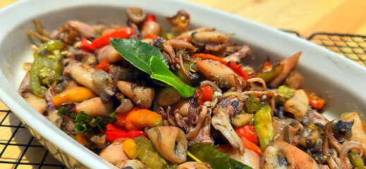 sauteed salty squid with black ink sauce with spicy seasoning called tumis cumi asin, is local Indonesian homemade cooking to include chili, ginger, and lime leaf served in a bowl