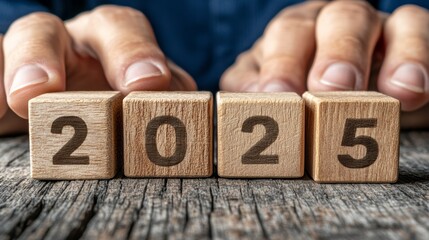 Closeup of hands arranging wooden blocks to spell out the year 2025.  A concept of new beginnings and anticipation for the future.