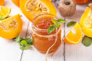 Golden pumpkin jam preserves. Sweet pumpkin and orange marmalade or confiture in small jar, with sliced pumpkin and mint on wooden kitchen table, copy space