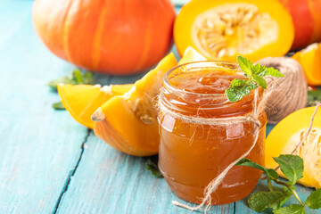 Golden pumpkin jam preserves. Sweet pumpkin and orange marmalade or confiture in small jar, with sliced pumpkin and mint on wooden kitchen table, copy space