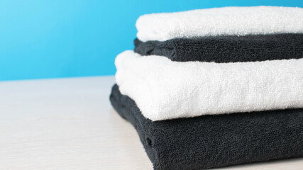 Stack of Black and White Towels on Light Wood Surface with Blue Background