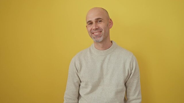Confident bearded hispanic guy exudes joy and luck, bald, proud man wearing sweater, flashing a perfect smile and laugh. standing against yellow isolated background with cool natural look