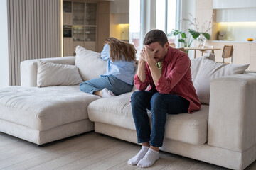 Crying woman turned away from husband, stressed man sitting with face covered with hands. Spouses...