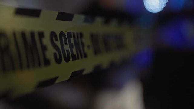 A close-up of a yellow crime scene tape with defocused lights in the dark background suggesting a nocturnal investigation.