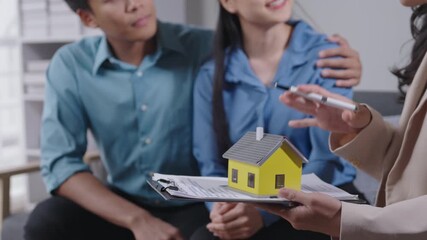 Excited couple consults with real estate agent, smiling and pointing at house model. Scenes show engagement in home buying process