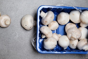 Raw mini mushroom champignon in a blue plastic box at gray background. Top view