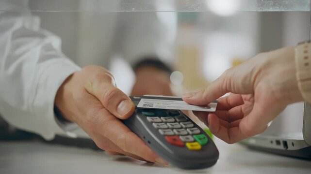 The client pays with a bank card by touching it to an electronic device. The pharmacist accepts non-cash payment from a buyer who purchased medications at the pharmacy