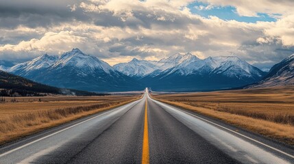Naklejka premium Straight highway with snow-capped mountains and cloudy skies, showcasing the beauty of nature and road trips.