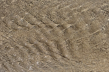 Sea water draining back to the ocean creating a ripple effect abstract background of the seaside beach