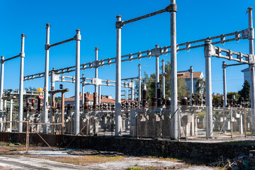 An old obsolete high-voltage transformer with a risk of voltage drops and power cuts. Electricity redistribution substation in A Coruña, Galicia, Spain. Blue sky and nearby homes