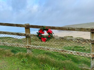 Christmas wreath with red bows on a wooden fence with the beach and sea behind