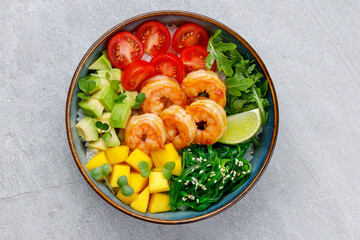 Poke bowl with shrimp, avocado, radish, carrot, tomato, chuka seaweed and white rice. Soy sauce, lime and sesame dressing. Green table background, top view