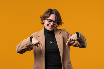Businesswoman pointing down, advertising area. Yellow background. 30s blogger asking to click to...
