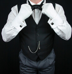 Butler or Hotel Concierge in White Gloves and Waistcoat Straightening Black Bow Tie. Professional Hospitality and Courtesy.