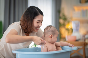 A woman is washing a baby in a blue bathtub. The baby is smiling and enjoying the experience. The woman is smiling and seems to be happy to be spending time with her child