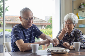 senior asian couple drinking tea together and talk in kitchen at home