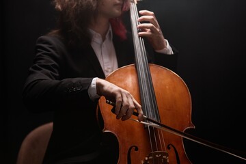 Cropped shot of unrecognizable male musician with long hair playing cello performing classical...