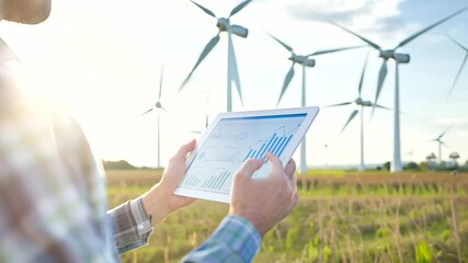 Close-up Energy analyst in wind farm with tablet showing energy graphs - Powered by Adobe