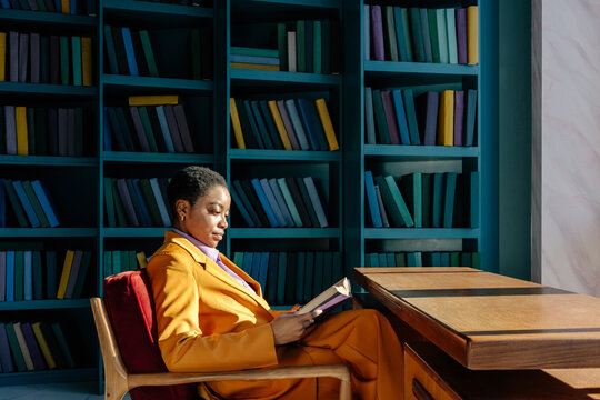 Woman reading book in armchair against book shelves