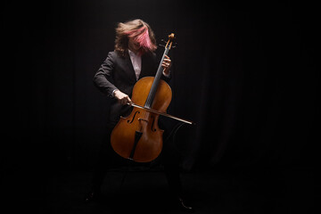 Shot of unrecognizable male musician with pink lock of long hair passionately playing cello on...