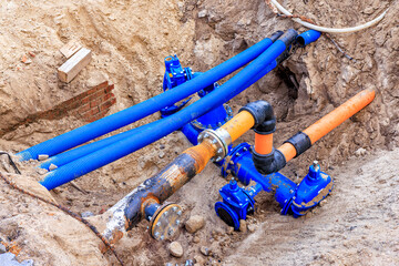 Blue and orange water pipes and cable conduits in a pit. Repair work is underway on city utilities.