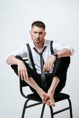 A man with white shirt and tie sits on a chair in studio. Barefoot