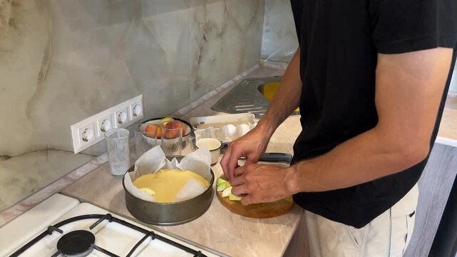 Man preparing homemade apple pie in modern kitchen, cutting apples and arranging them on pie crust. Detailed steps in baking process shown