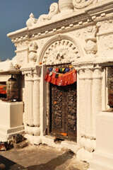 The elaborate entrance door, gate of the Boudhanath Stupa, decorated with carvings, sculptures, prayer flags and prayer wheels, Kathmandu, Nepal