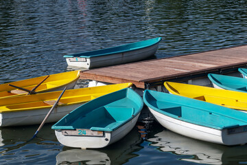 Colorful boats, yellow and blue, moored at a wooden dock on a body of water, with one boat featuring a paddle