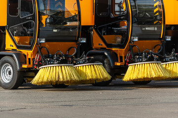 A parking area for street cleaning machines with large yellow brushes lined up for street cleaning