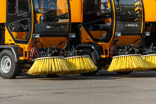 A parking area for street cleaning machines with large yellow brushes lined up for street cleaning