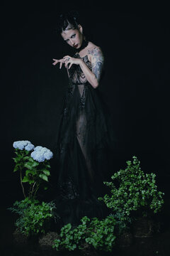 Sinister woman in a black dress in a set with plants and flowers