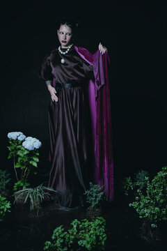 woman with purple dress and cape in aa set made of plants and flowers 