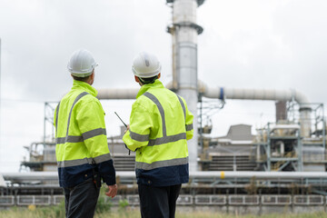 Two male petrochemical engineers with walkie-talkie working and discussing inspection and maintenance plans for pipelines for oil and gas at petroleum refinery, power plant energy industry.