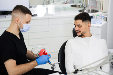 Teeth cleaning technique demonstration by dentist. Doctor teaches patient how to clean his teeth in...